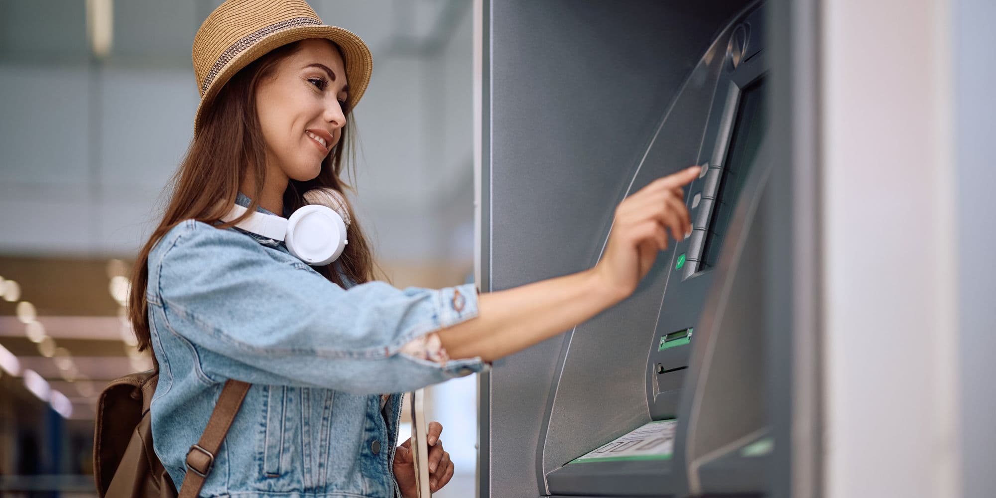 młoda kobieta turystka w kapeluszu słomkowym wypłacająca pieniądze z bankomatu